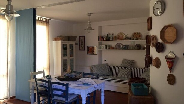 A dining area with a table and chairs, a sofa, and a bookshelf with various items. - A Pochi Passi dal Mare di Marciana Marina (Marciana Marina)
