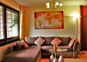 A living room with a sectional sofa, a glass coffee table, and a world map painting on the wall. - Weststadtblick (Heidelberg)