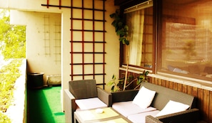 A room with a tatami mat floor, a low wooden table, two wicker sofas with cushions, a large window with a view, and a shoji screen. - Weststadtblick (Heidelberg)
