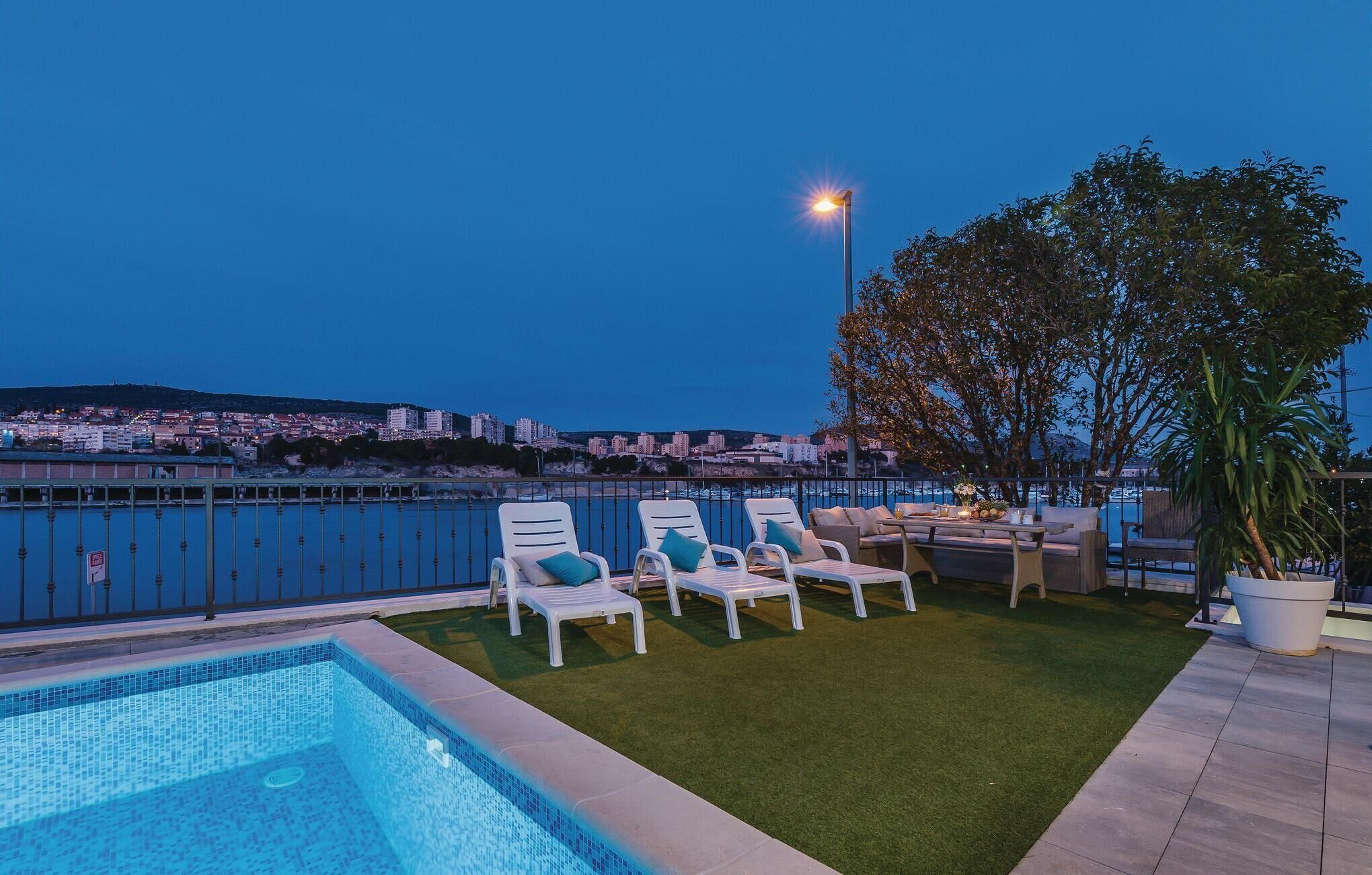 Zona de piscina en la azotea con sillones de descanso y un pequeño espacio de estar, con vistas a un paisaje urbano.