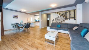 A modern living room with a grey sofa, a coffee table, and a dining area with chairs and a table. - Amazing home in Sibenik (Sibenik)