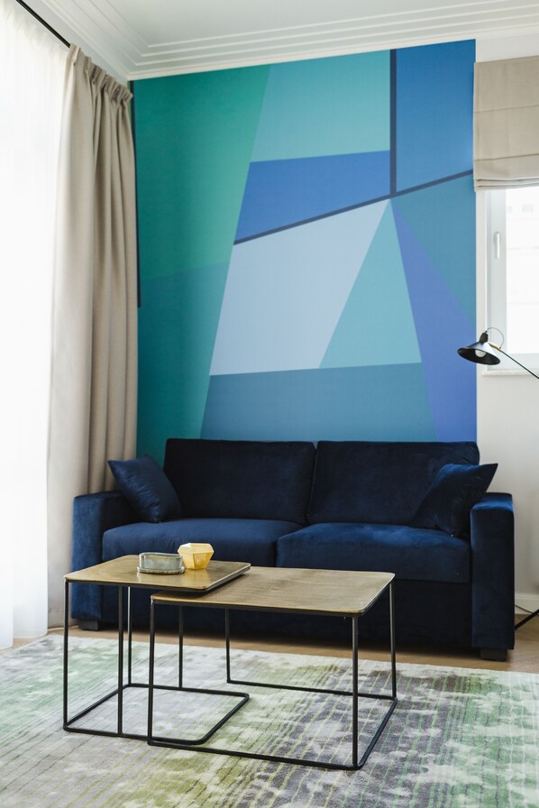 Una sala de estar moderna con un sofá azul, una mesa de centro de madera y un mural geométrico en la pared.