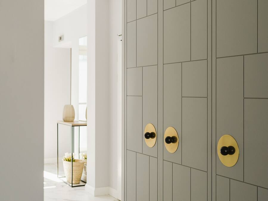 A hallway with a grey tiled wall, a white floor, and a door with a circular handle.