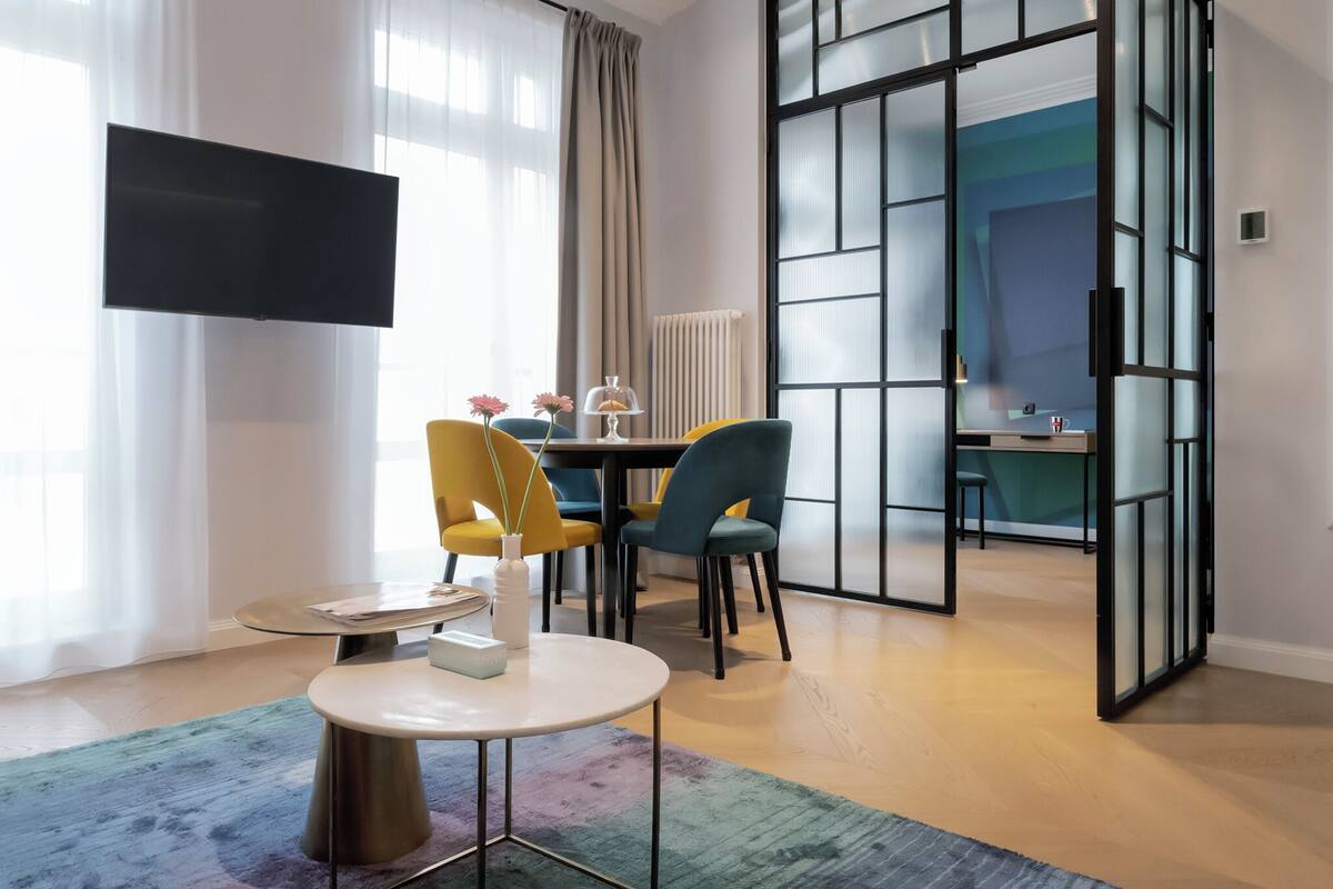 Habitación de hotel moderna con comedor, televisor de pantalla plana en la pared y vistas a través de un separador de vidrio.