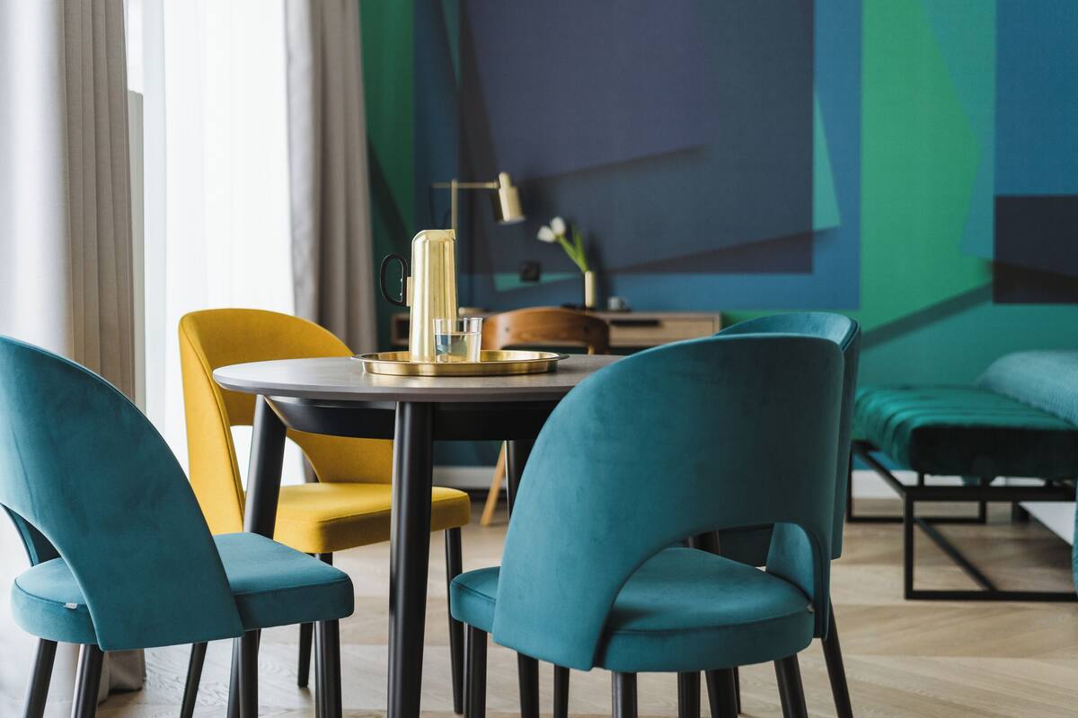 Un comedor moderno con sillas azul verdosas y amarillas, una mesa redonda y una lámpara decorativa.