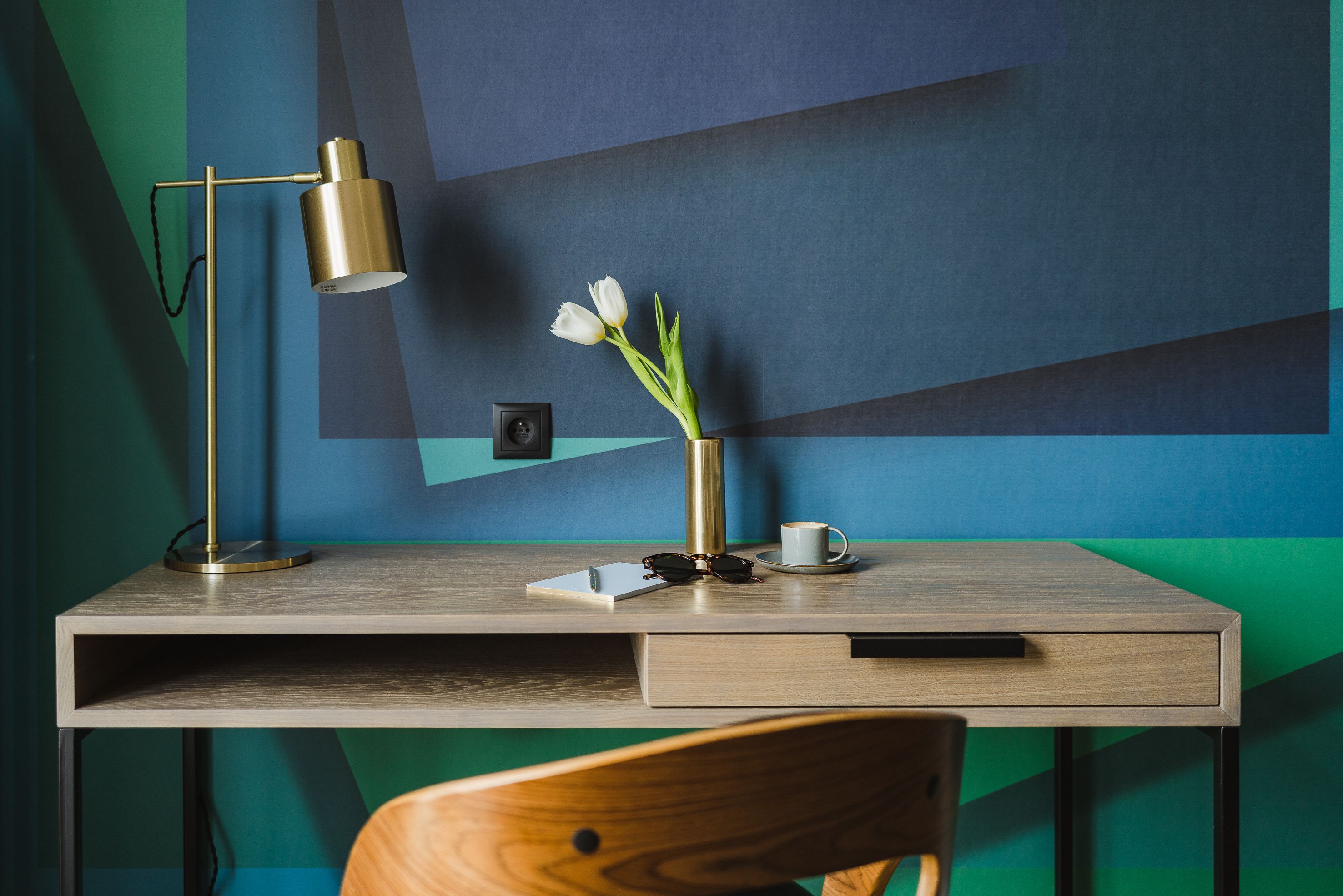 A modern desk with a lamp, a vase with flowers, a cup, and a pair of sunglasses.