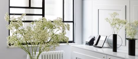 A modern kitchen with a round glass table, white cabinets, and a vase of white flowers on the counter.