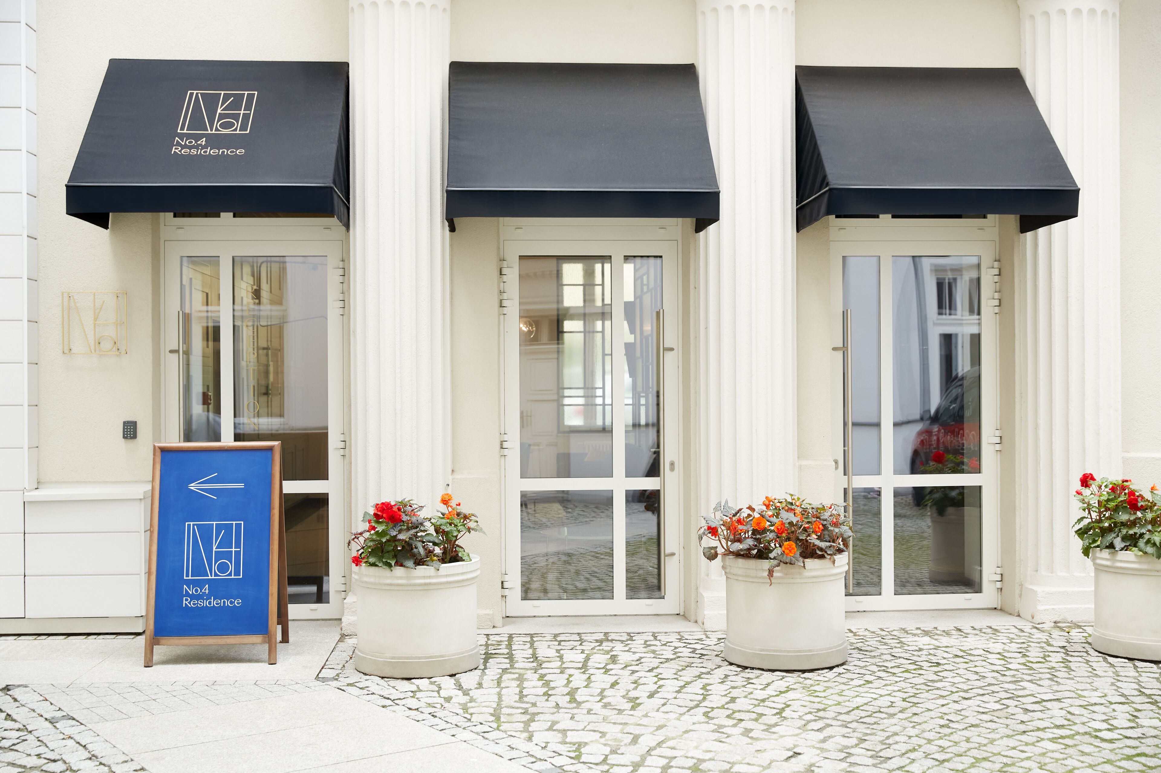 A building with three black awnings, a glass door entrance, and potted plants.