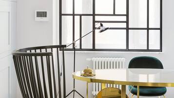 Ein moderner Essbereich mit einem schwarzen Stuhl, einem goldenen Tisch und einem großen Fenster mit geometrischem Muster.