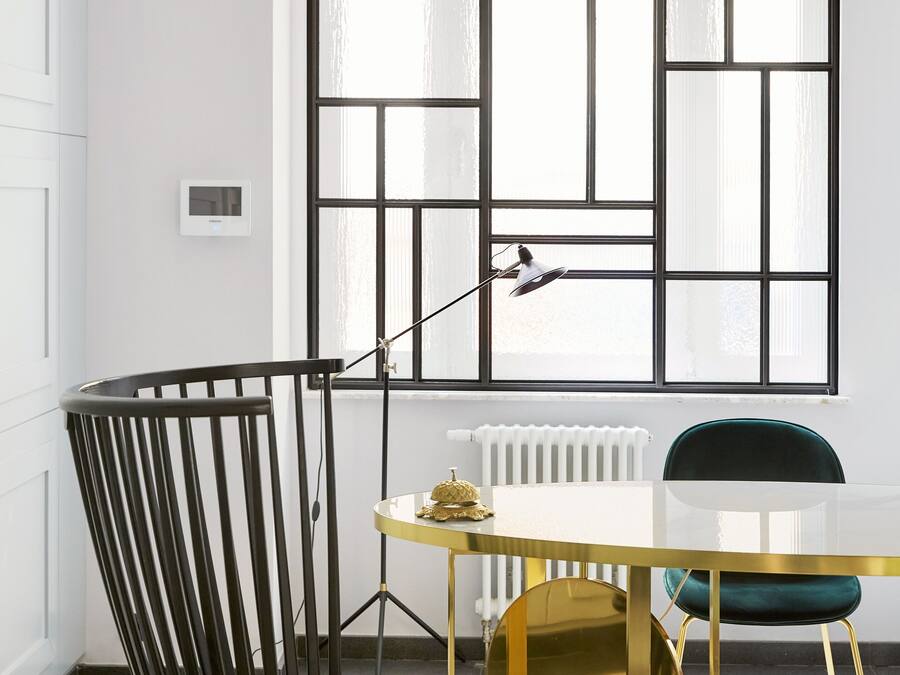 Ein moderner Essbereich mit einem schwarzen Stuhl, einem goldenen Tisch und einem großen Fenster mit geometrischem Muster.