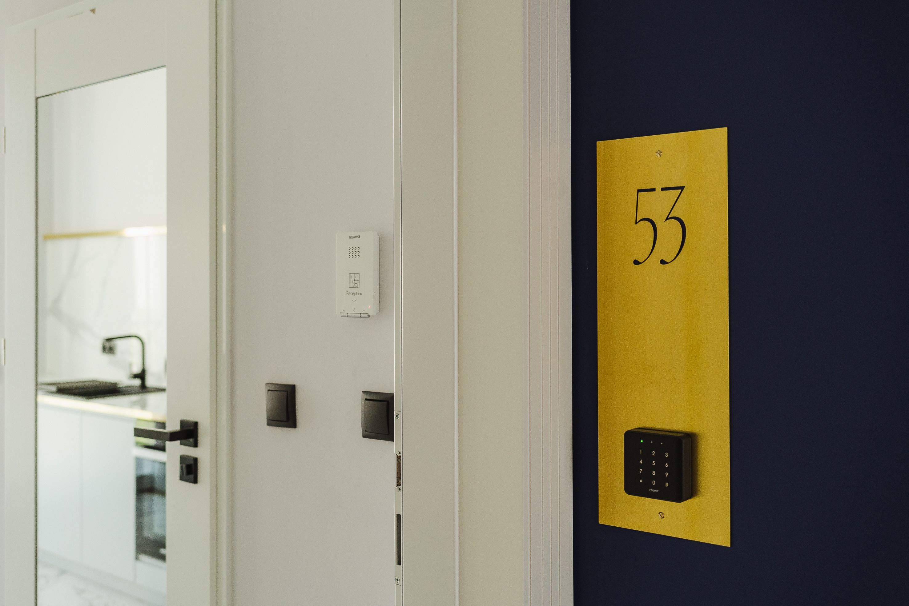 A hotel room with a door, a wall-mounted number plate, and a keypad lock.