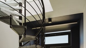 A spiral staircase with metal railings and a view of a residential building through a large window. - No.4 Residence (Warsaw)