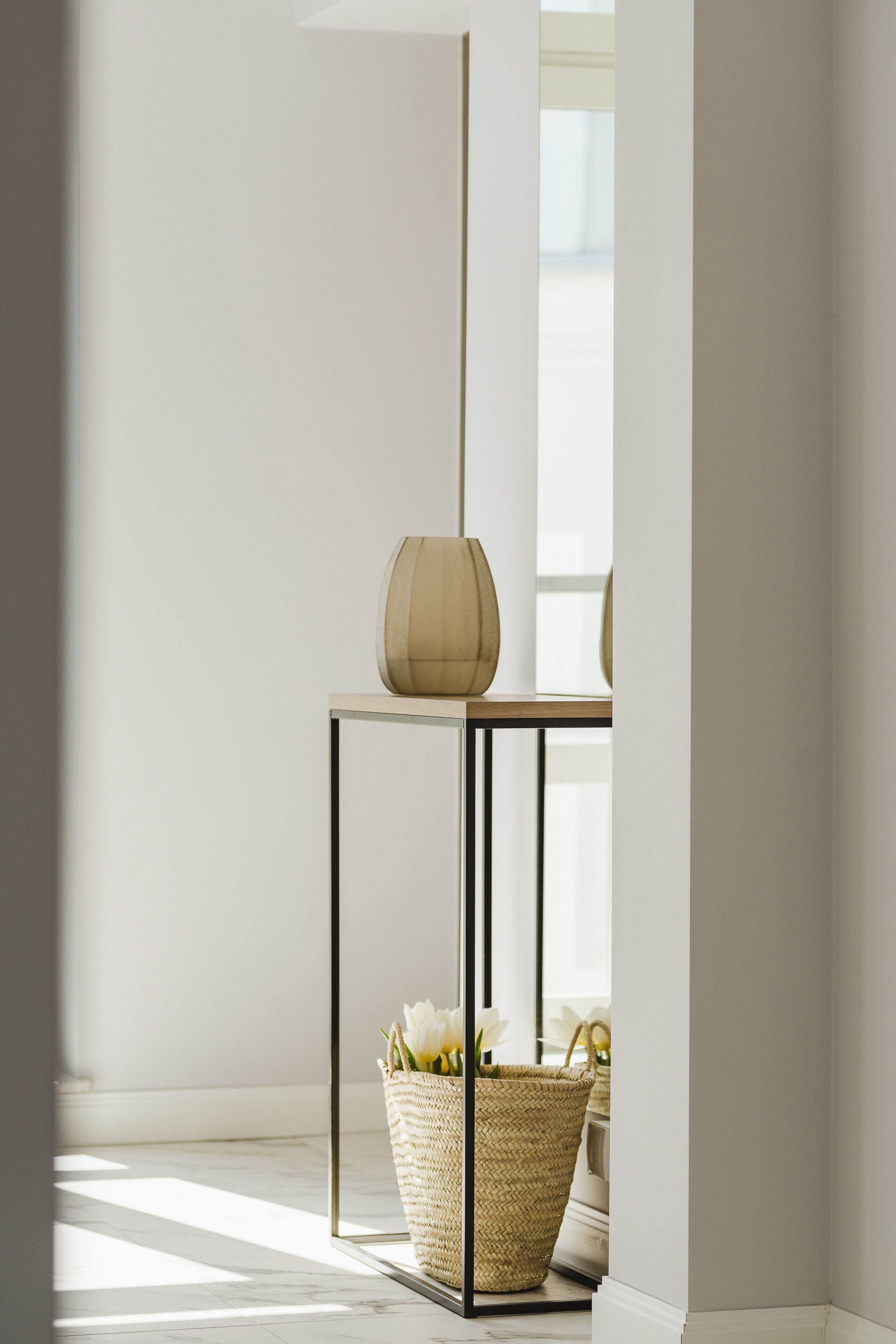 A minimalist room with a table, a vase, and a basket with flowers.