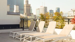 A rooftop terrace with white lounge chairs and a city skyline in the background. - No.4 Residence (Warsaw)