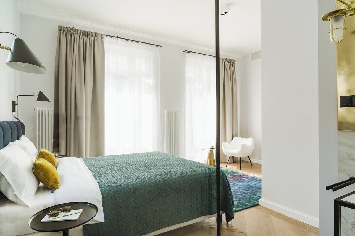 Habitación de hotel moderna con cama, mesita de noche, lámpara y vistas a la ciudad.