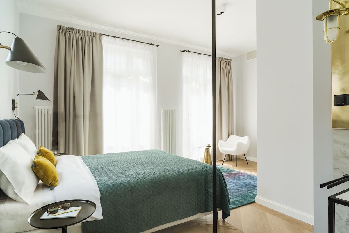 Habitación de hotel moderna con cama, mesita de noche, lámpara y vistas a la ciudad.