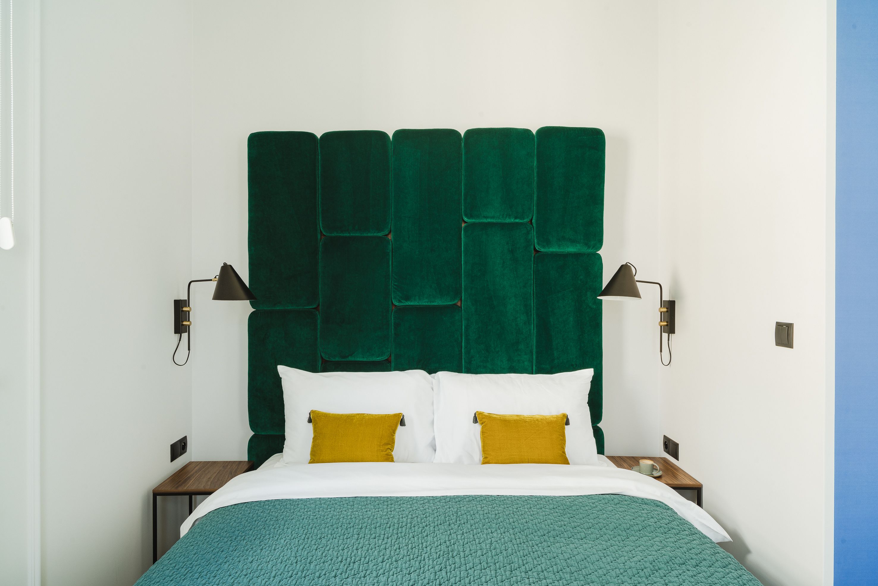 A hotel room with a green upholstered headboard, white bedding, and two bedside lamps.