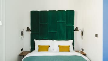 A hotel room with a green upholstered headboard, white bedding, and two bedside lamps.