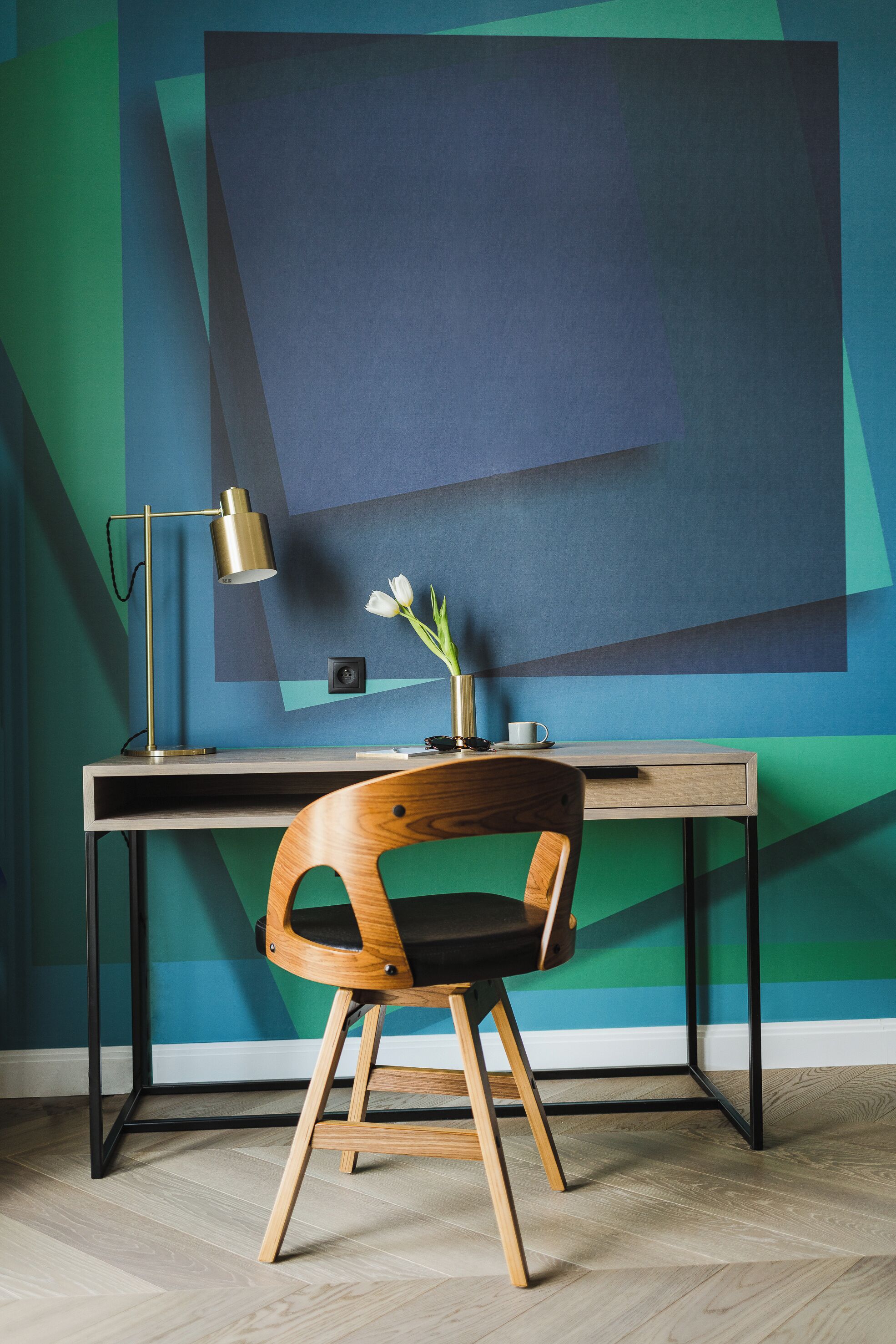 A modern office desk with a lamp, a vase with flowers, and a chair.