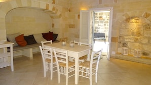Un coin repas chaleureux avec un mur en pierre, une table en bois et des chaises blanches.