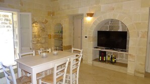 Un coin repas avec un mur en pierre, un téléviseur fixé au mur et une table avec des chaises.