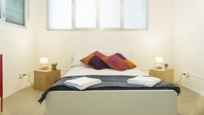 A neatly made bed with two pillows, two bedside tables with lamps, and a window above the bed. - Hostelleria (Trapani)