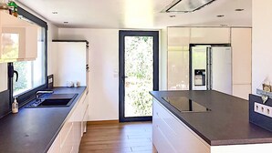 Eine moderne Küche mit einer großen Kochinsel, eingebauten Geräten und einer Schiebeglastür, die auf einen Balkon führt.