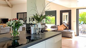 Eine moderne Küche mit Kochinsel, ein Essbereich mit gestreiften Stühlen und ein Wohnzimmer mit Sofa und Fernseher.