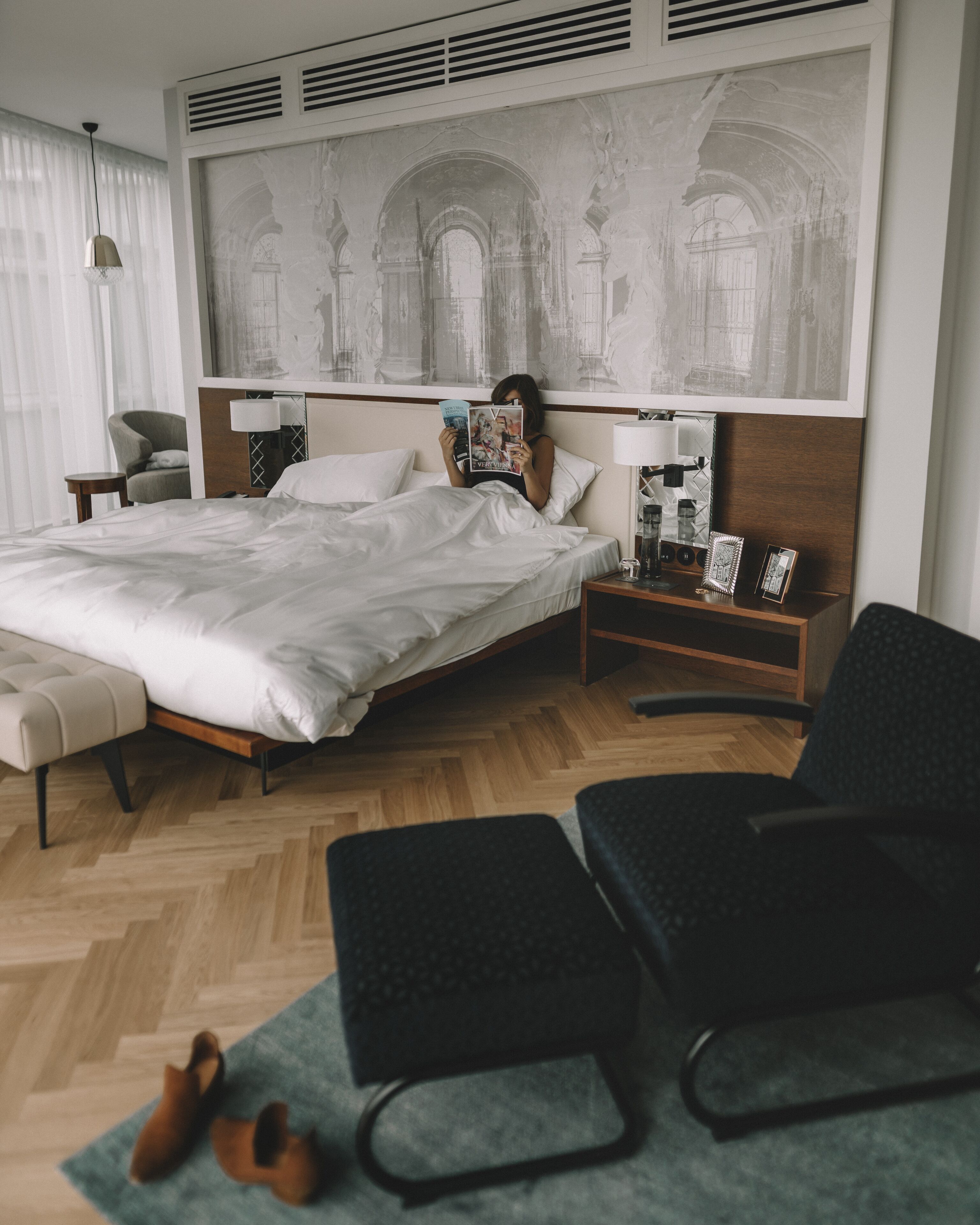 Una habitación de hotel moderna con una cama grande, un sillón de lectura, un escritorio y un mural grande en la pared.