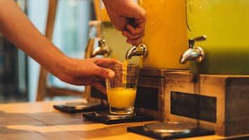 En hand häller apelsinjuice från en kran ner i ett glas.