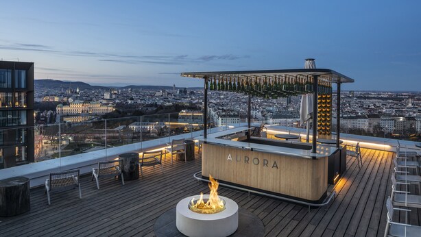 Un bar situé sur le toit, doté d’un foyer, d’un comptoir et d’un espace salon offrant une vue panoramique sur la ville.