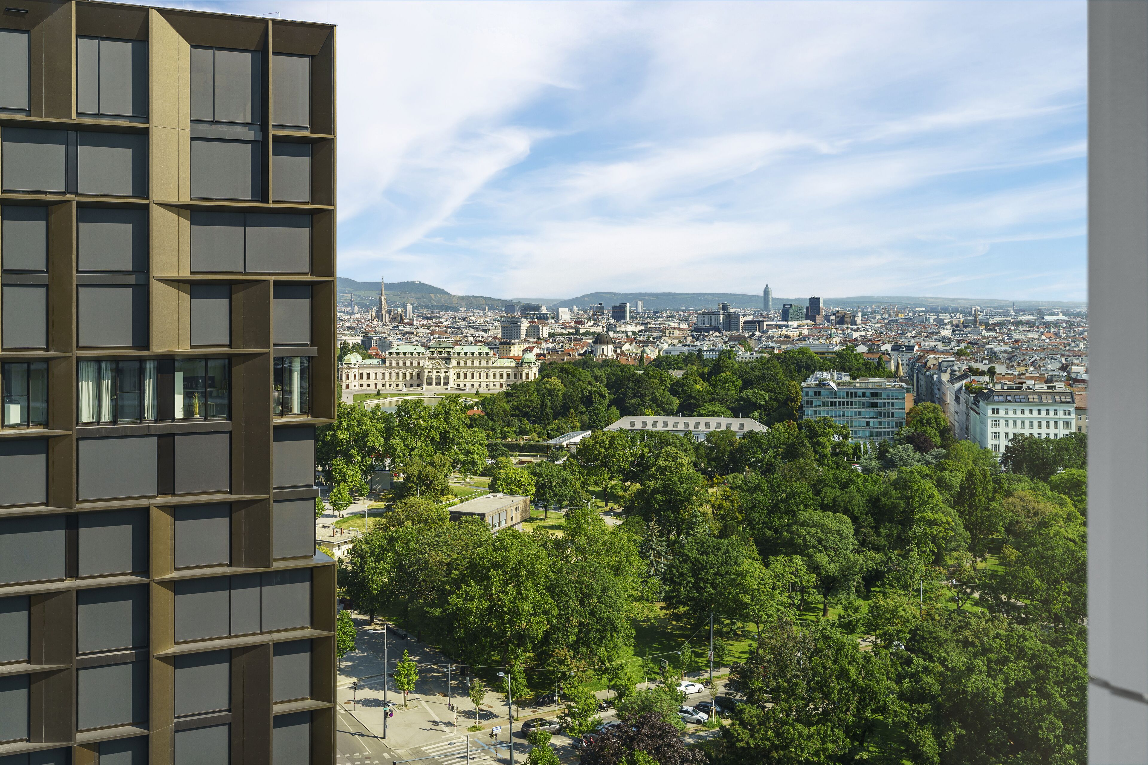 A high-rise building with a grid-like facade and a view of a cityscape with various buildings and greenery.