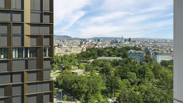 A high-rise building with a grid-like facade and a view of a cityscape with various buildings and greenery.