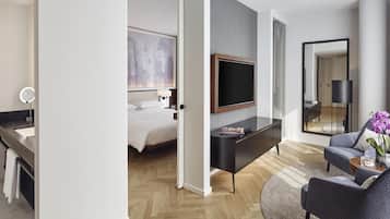 A modern hotel room with a bed, a TV, a desk with a mirror, a chair, and a large mirror.