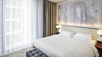 A hotel room with a large bed, a nightstand with a lamp, a window with sheer curtains, and a wall mural.