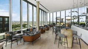 Un espace lounge moderne doté de grandes fenêtres, d’un bar en bois et de sièges confortables.