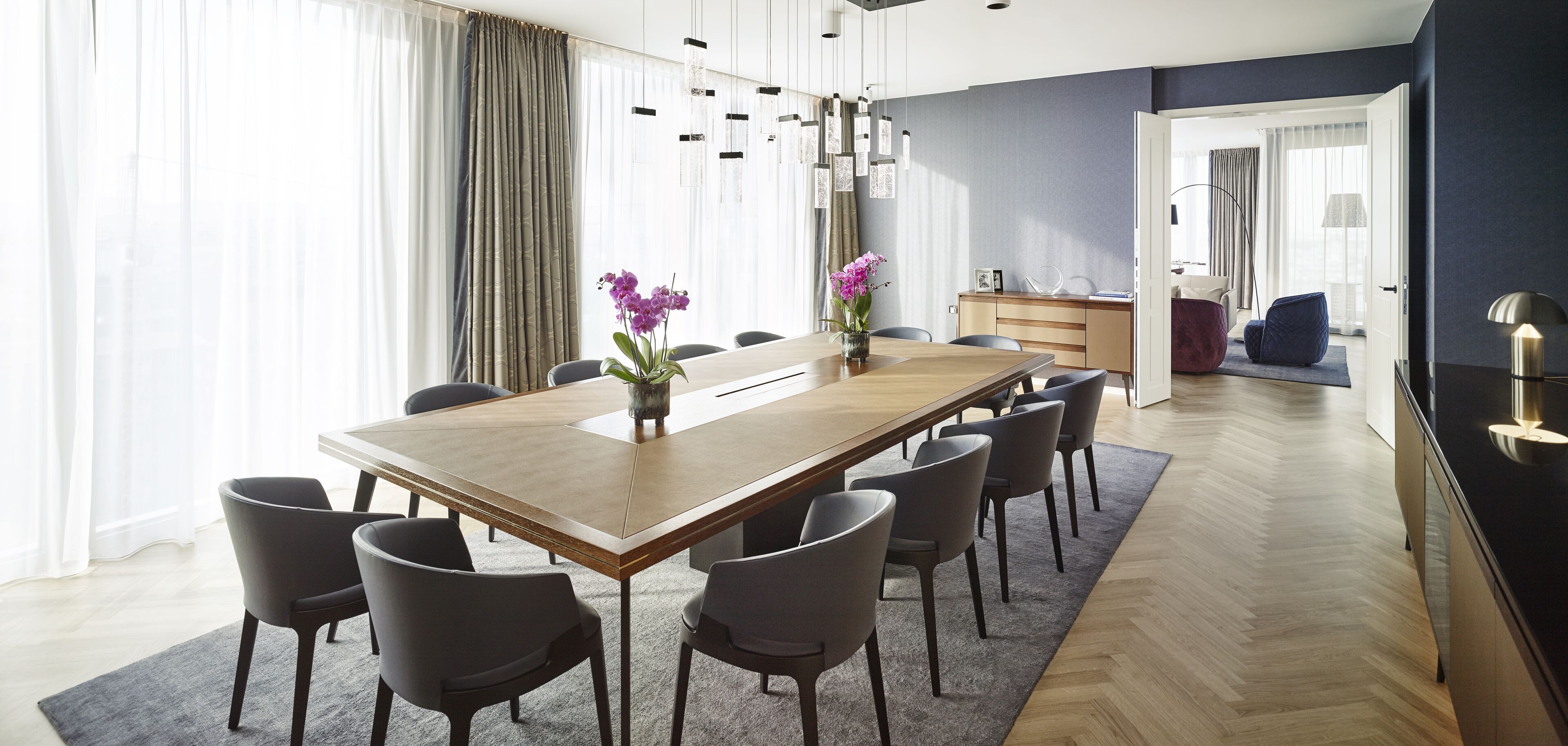 Een moderne eetruimte met een lange houten tafel, verschillende stoelen en een bloemenvaas.