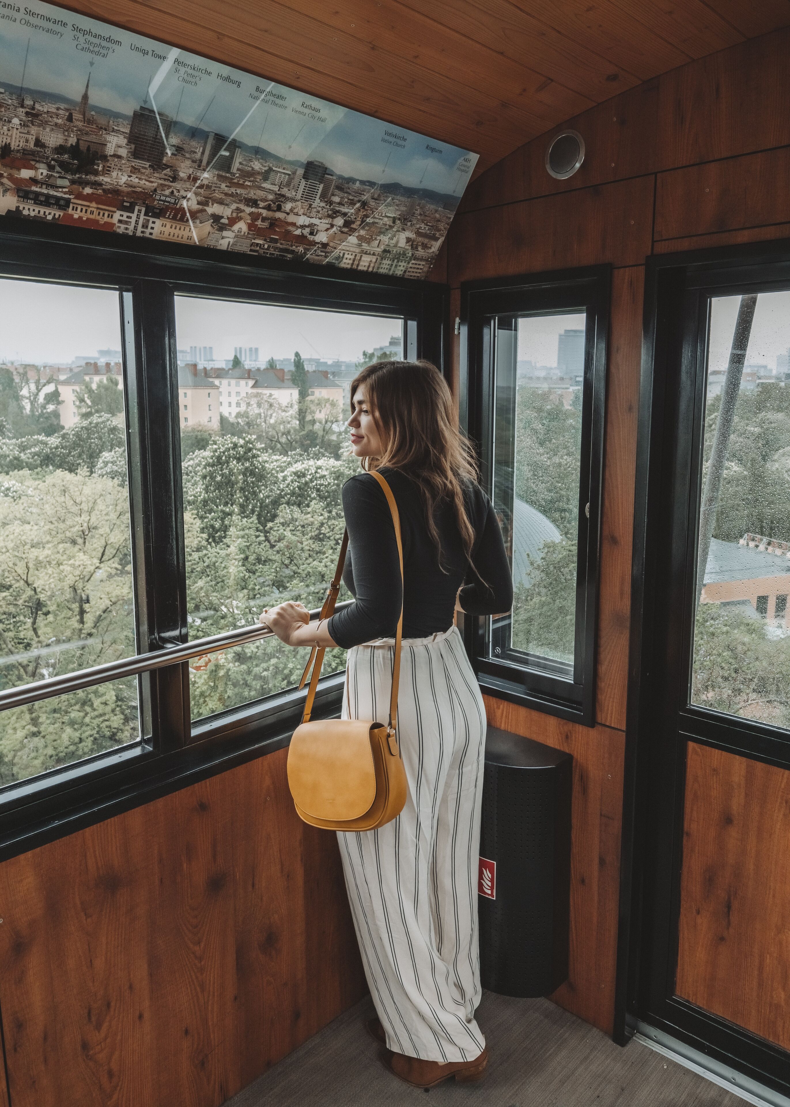 A person standing by a window with a cityscape view, holding a bag.