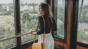 A person standing by a window with a cityscape view, holding a bag.