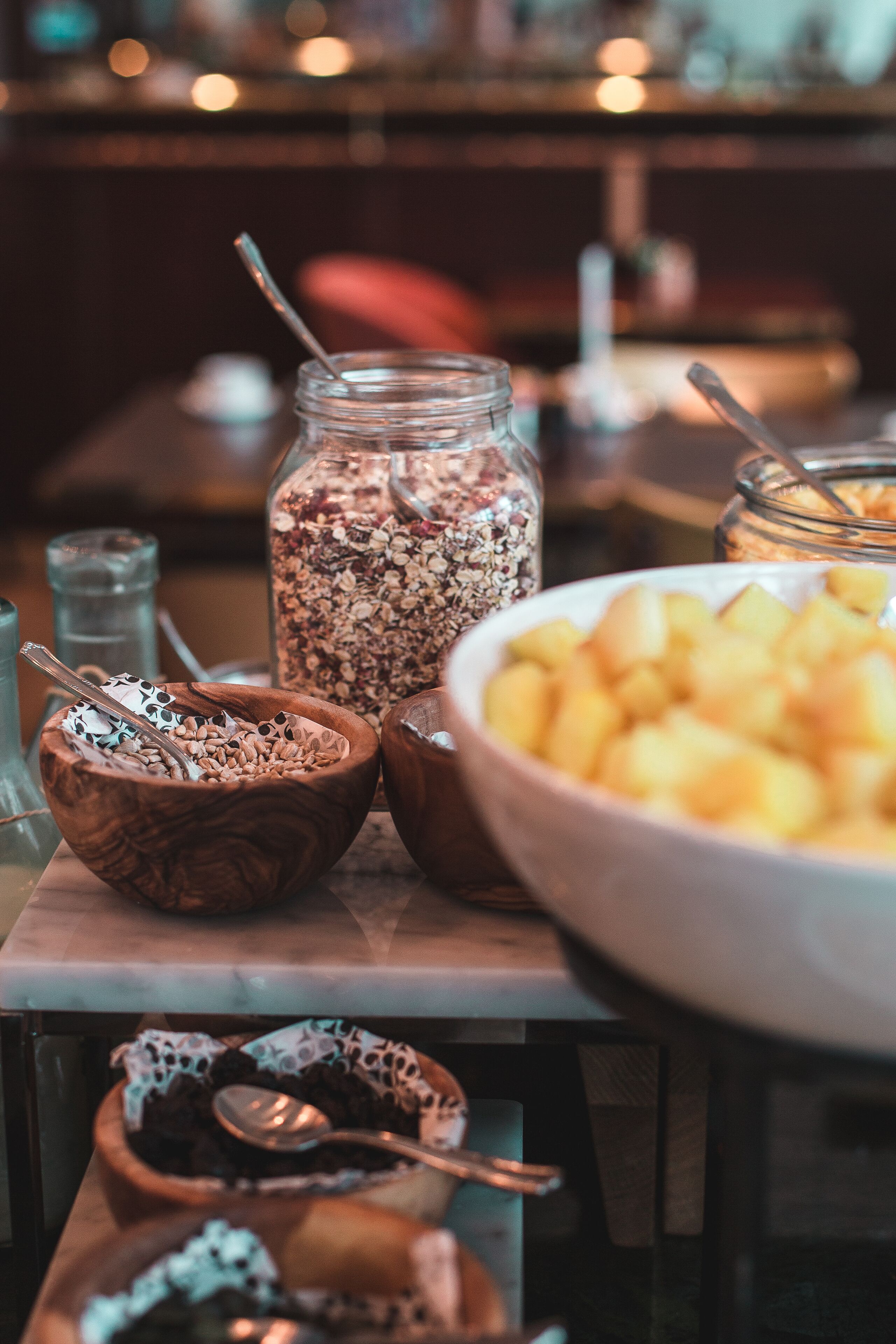 Une table sur laquelle on trouve divers aliments, notamment des bols de granola, un bocal de fruits secs mélangés et un saladier de fruits coupés en dés.