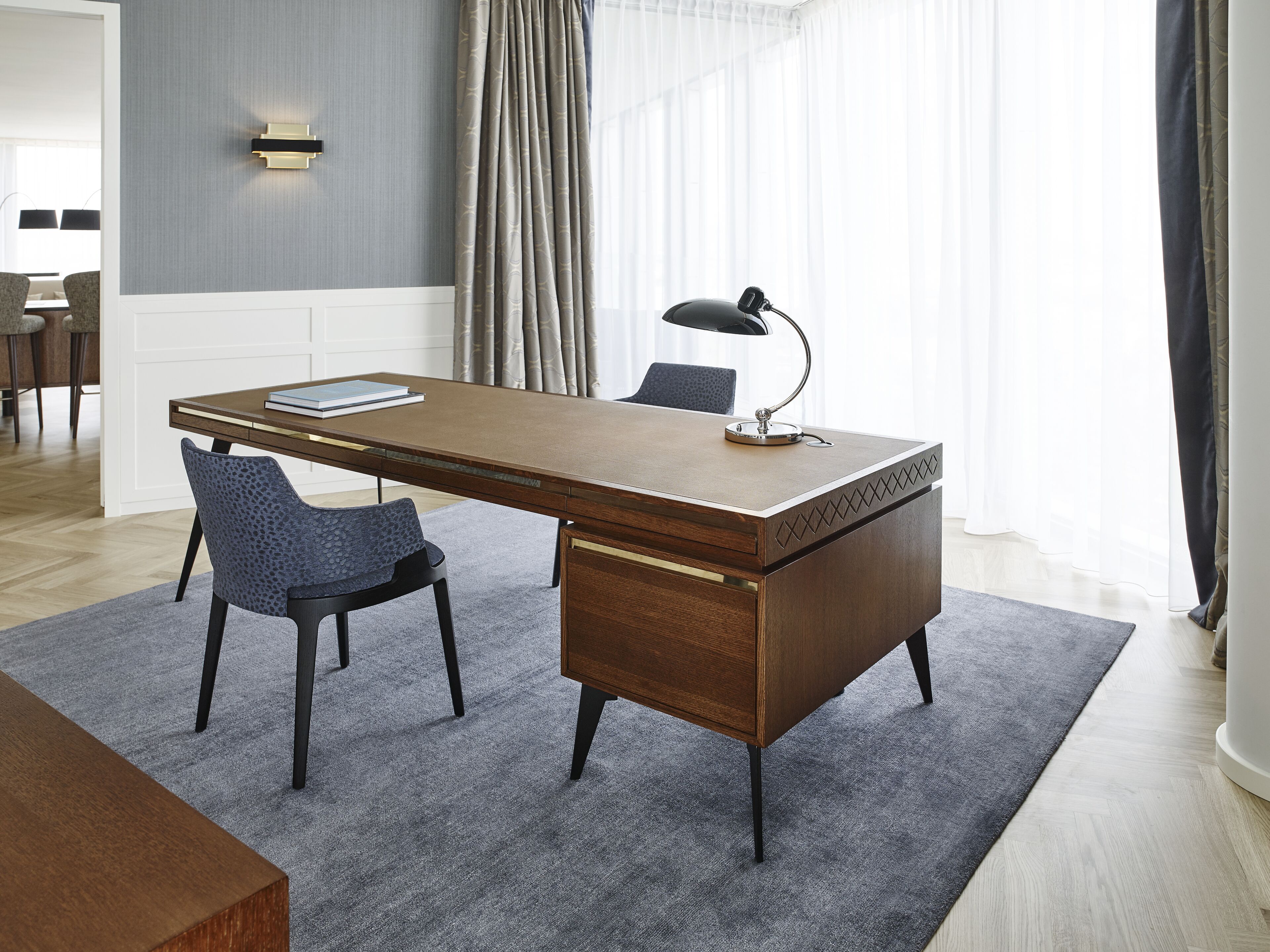 A modern office desk with a lamp, two chairs, and a book.