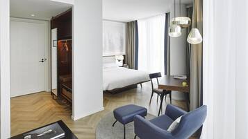 Quarto de hotel com cama, escrivaninha com cadeira, guarda-roupa e banheiro visível por uma porta aberta.