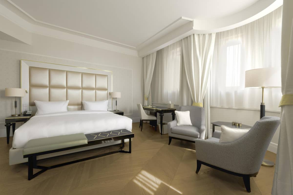 A modern hotel room with a large bed, a desk, a chair, and a sofa.