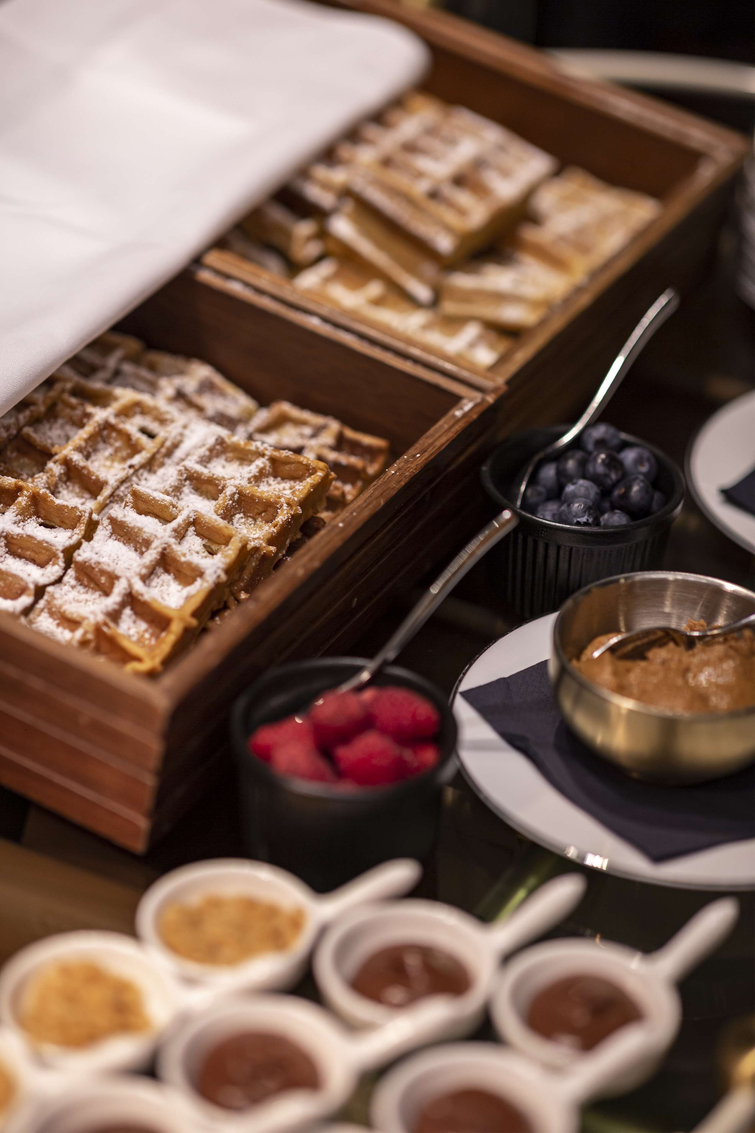Un buffet con waffle, mirtilli, lamponi e diverse salse.