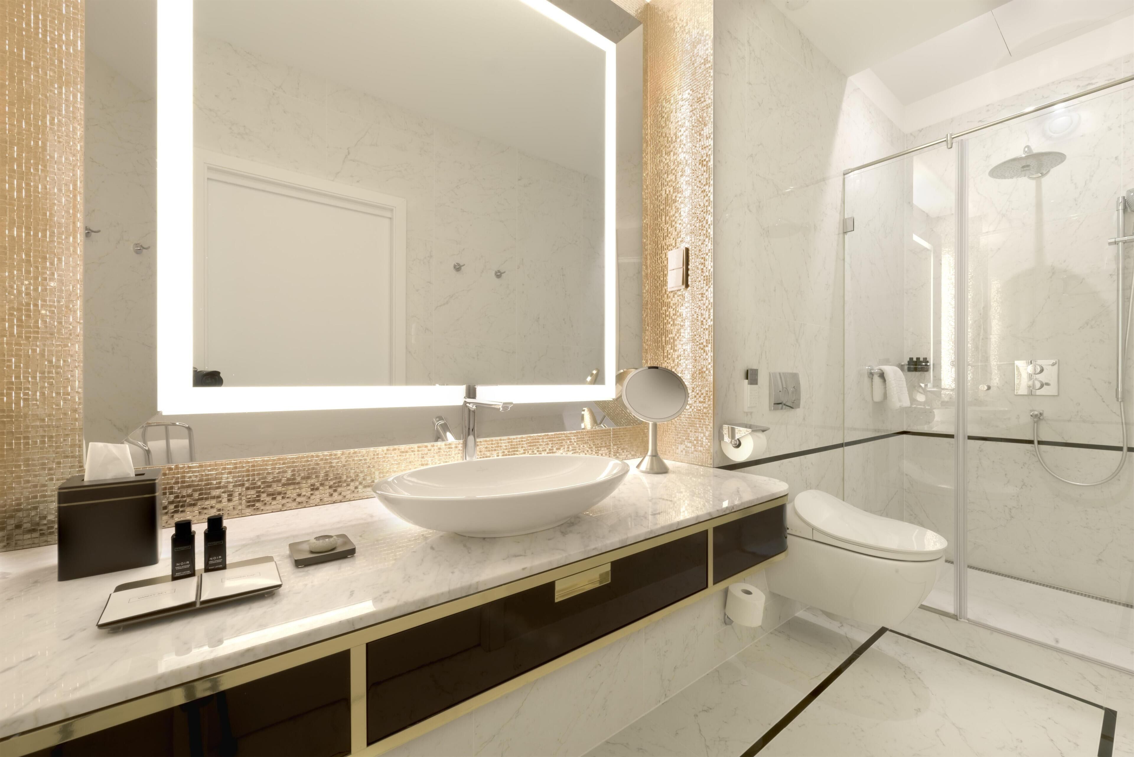 A modern bathroom with a large mirror, a sink, a toilet, and a glass-enclosed shower.