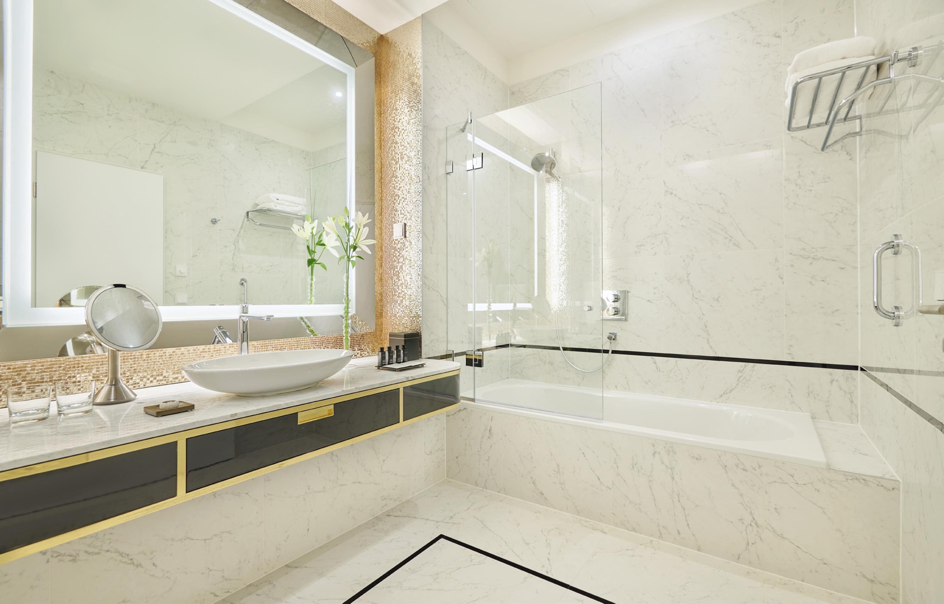 Un baño moderno con un espejo grande, un lavamanos blanco, una bañera y una zona de ducha con mampara de vidrio.