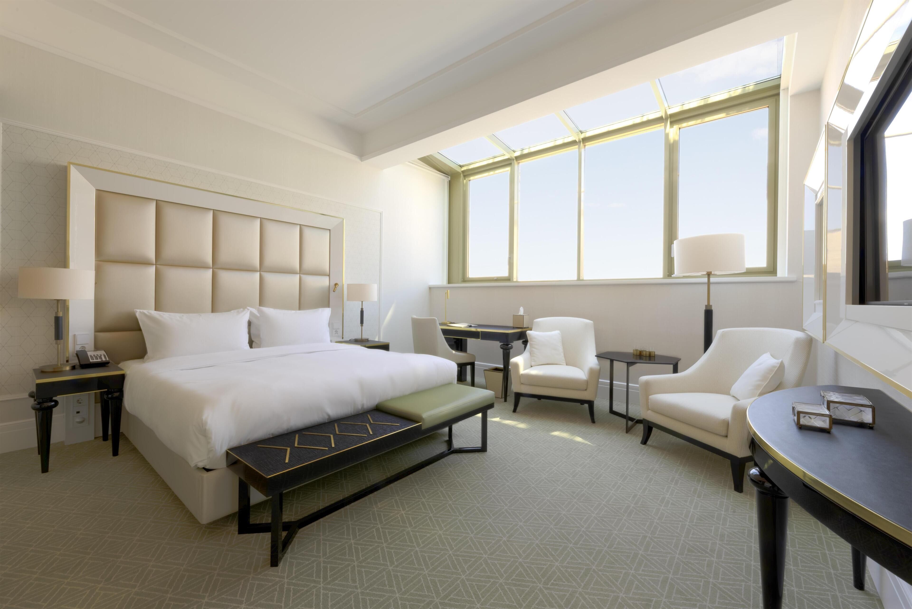 Habitación de hotel con una cama grande, un escritorio, una silla y un sofá. Ventanas que ofrecen luz natural.