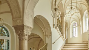 Una gran escalera con barandillas y columnas ornamentales, que conduce a un techo alto con molduras decorativas y candelabros.