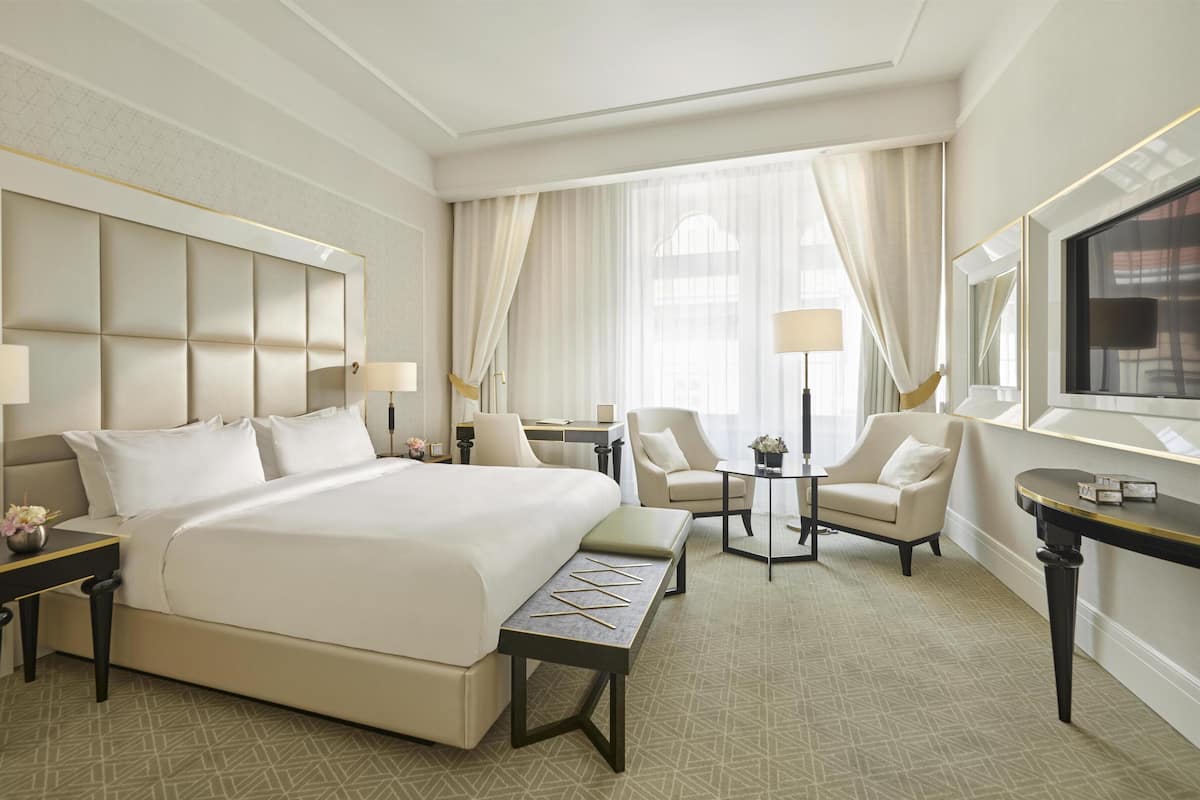 A hotel room with a large bed, two armchairs, a small table, a desk, and a TV.
