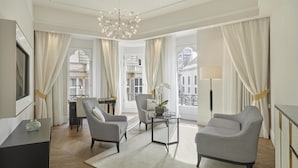 A modern hotel room with a large window, a chandelier, two armchairs, a small table, and a desk with a lamp. - Párisi Udvar Hotel Budapest, part of Hyatt (Budapest)